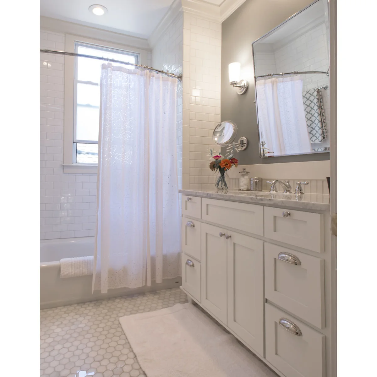 Compact bathroom with a curved shower-curtain rod, white tub and white vanity beside a grey wall