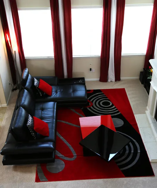 A black sectional sits on a red-and-black patterned rug beside tall windows.