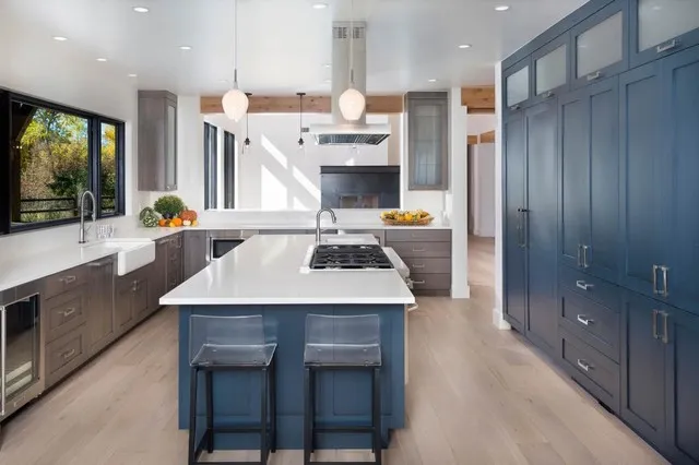 A full-height blue cabinet wall stands beside a blue island in a bright kitchen.
