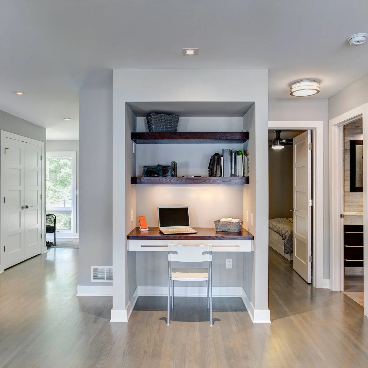 Small recessed desk between doorways with a white chair, two wood shelves and a laptop