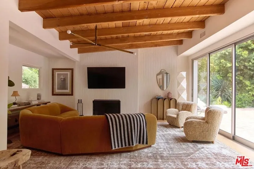 A warm-colored sofa sits beneath a timber ceiling beside pale textured chairs.