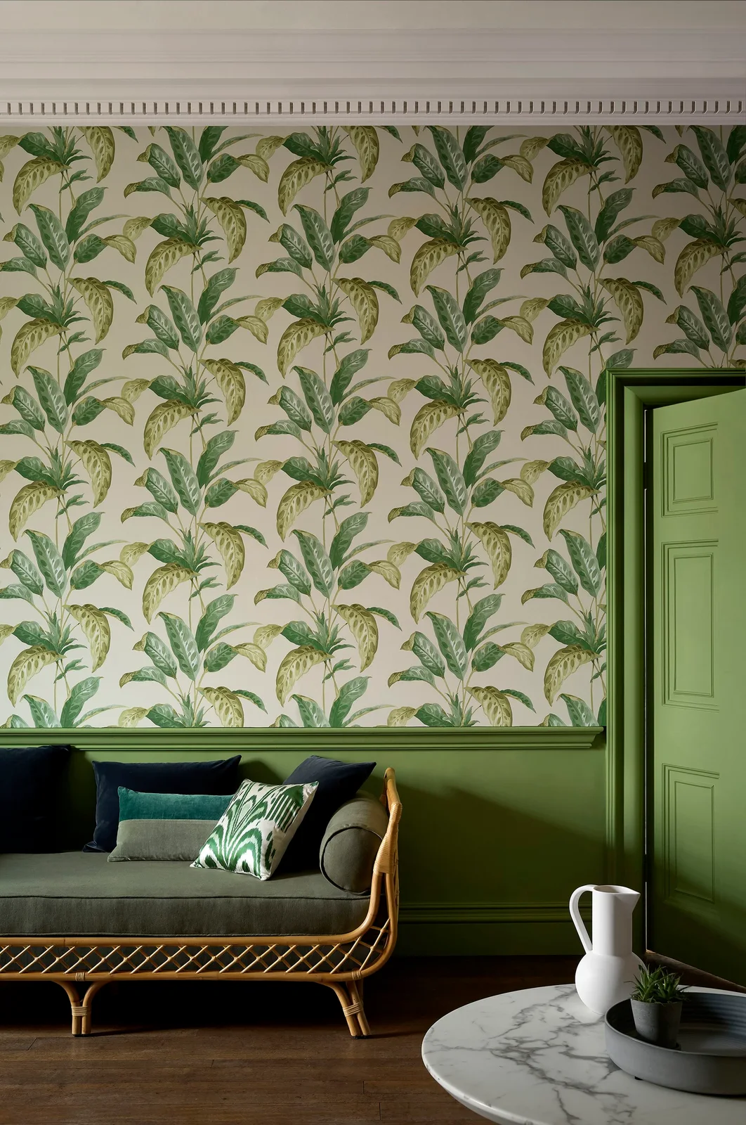 Green leafy wallpaper sits above green lower paneling beside a gray sofa and green-painted door.