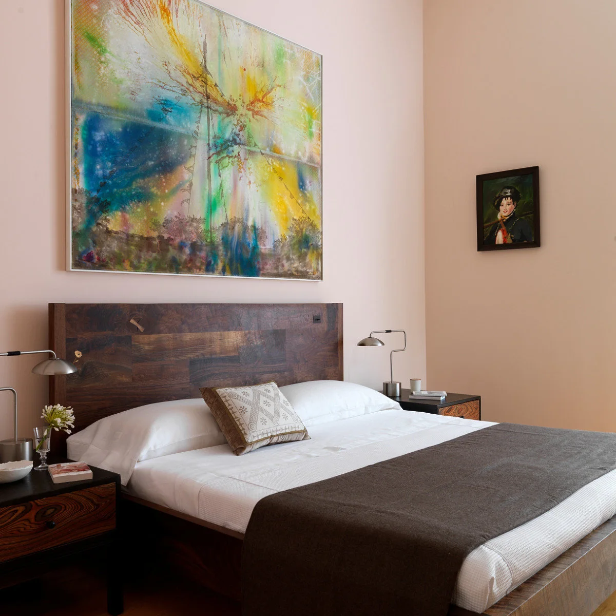 Large blue, yellow and green abstract painting above a wooden headboard in a pale pink bedroom.