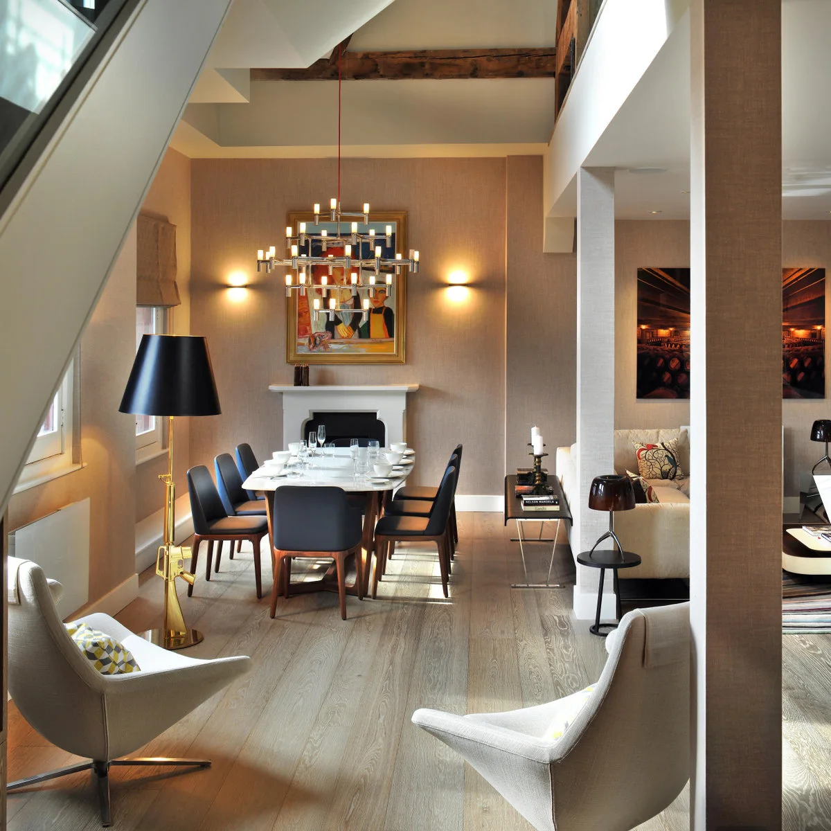 Loft interior with a dining table at the end of a narrow strip, pale lounge chairs in the foreground and a sofa beyond columns on the right.