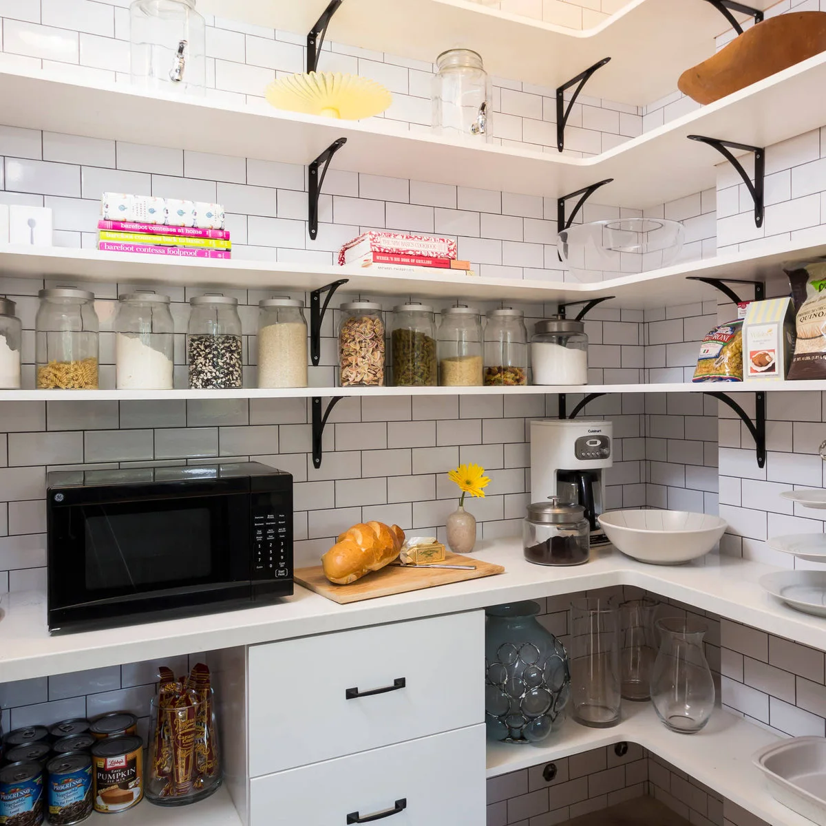 White pantry counter beneath open shelves with glass jars, a microwave and coffee maker