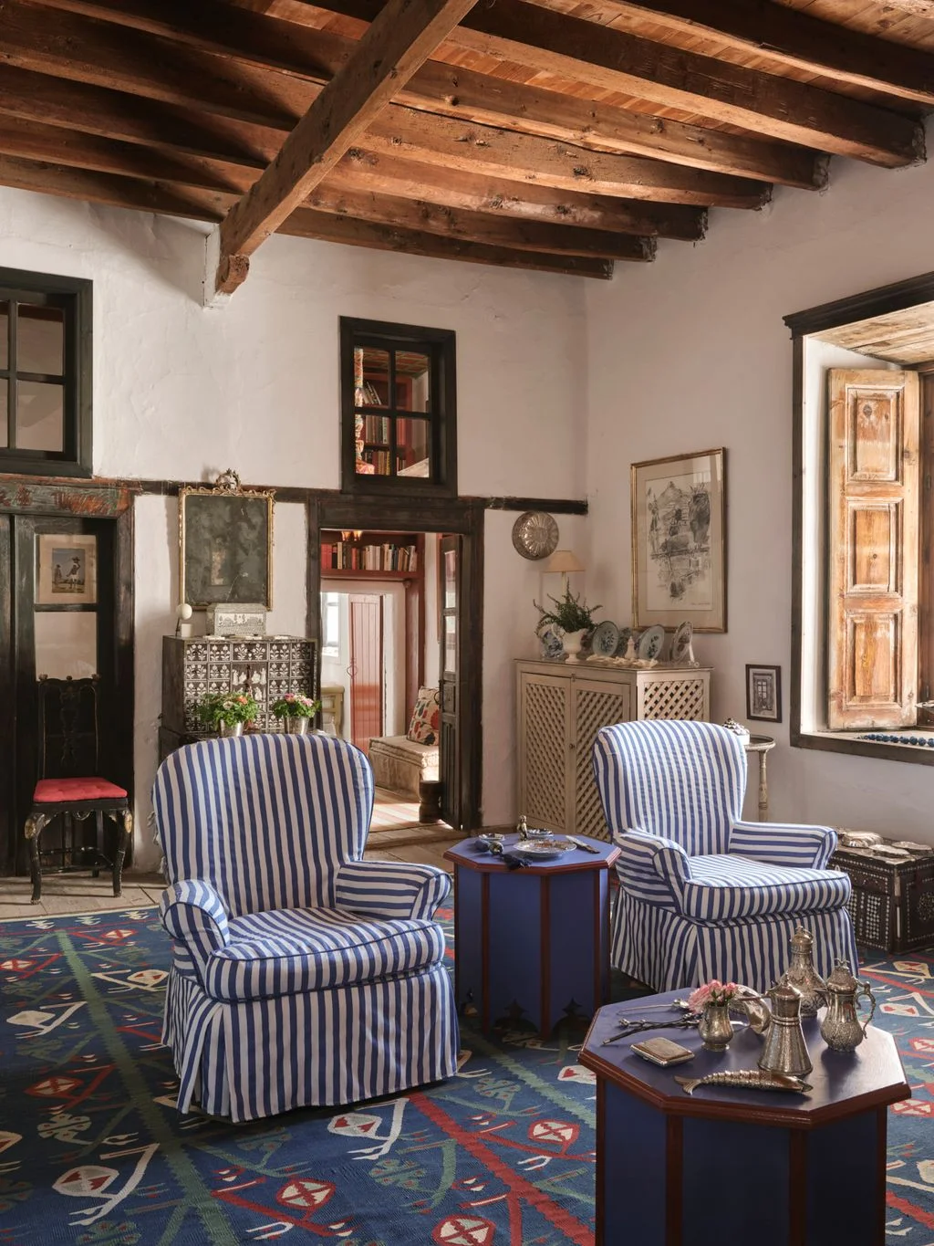 Two blue-and-white striped armchairs with small dark tables in a timber-beamed sitting room