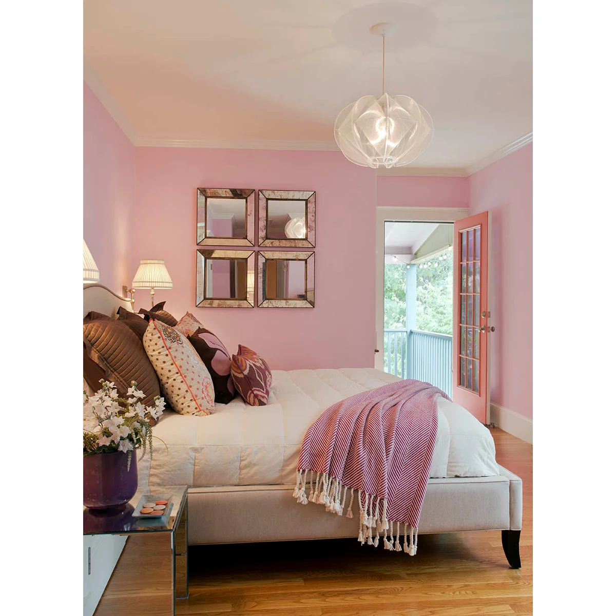 Pink-walled bedroom with pale upholstered bed, patterned cushions and a striped throw