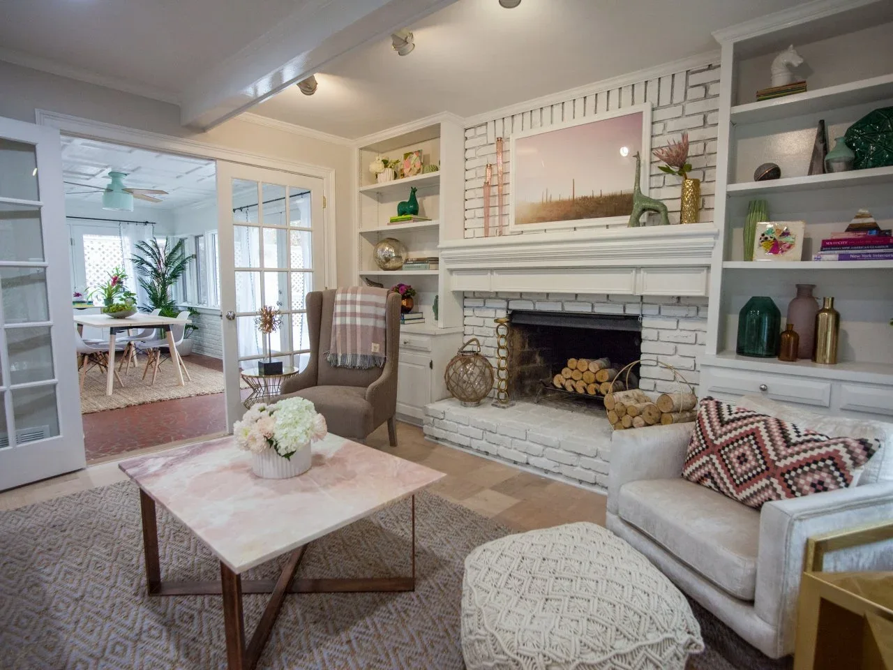 Pale brick surrounds a fireplace between white shelves, with a taupe chair and patterned upholstered seating nearby.