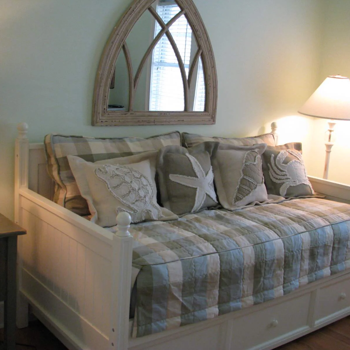 A white daybed holds pale striped bedding and sea-creature cushions beneath an arched mirror.