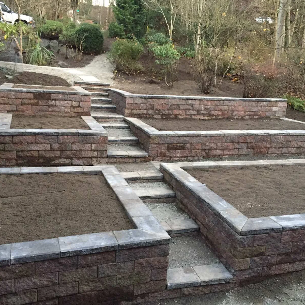 Tiered block retaining beds flank a narrow central garden staircase, with bare soil ready for planting.