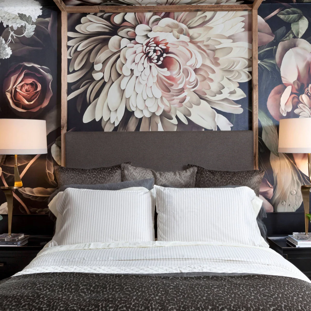 Large pale floral mural behind a gray headboard and wooden canopy bed with matching bedside lamps.