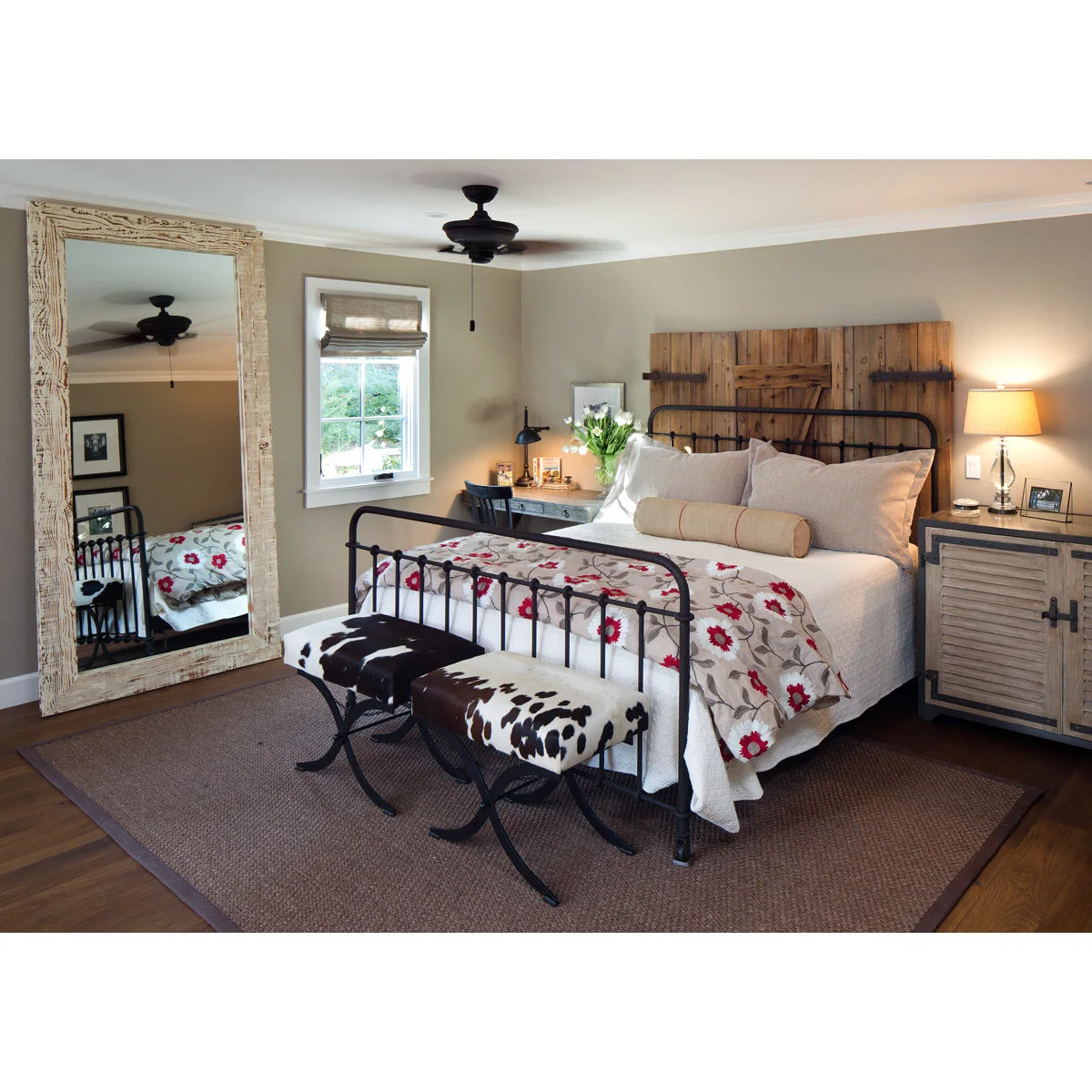 Bedroom with a black iron bed, wood barn-door headboard backdrop, floral bedding and two spotted stools