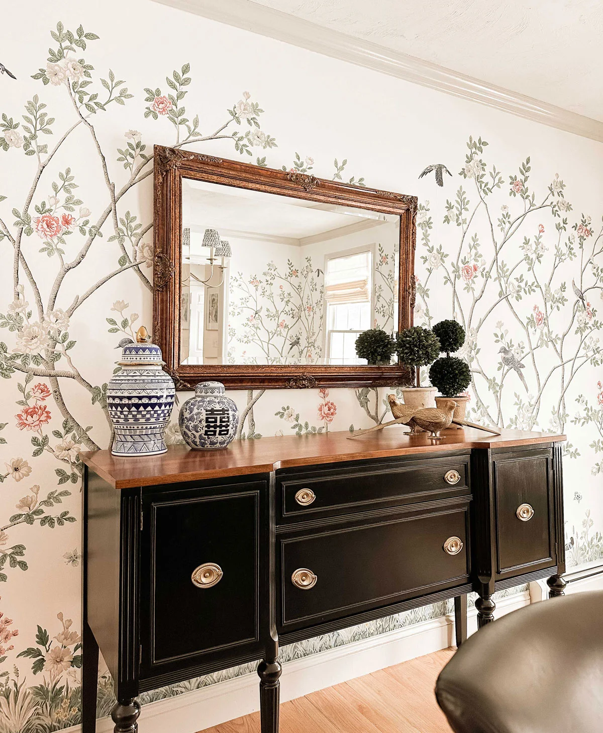 A dark sideboard with a wood top carries two blue-and-white jars at one end and rounded green forms and a bird ornament at the other.