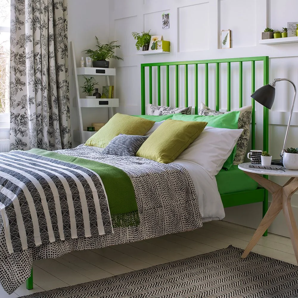 A bright green open headboard and bed frame sit beside white walls, black-and-white patterned bedding and small green accessories