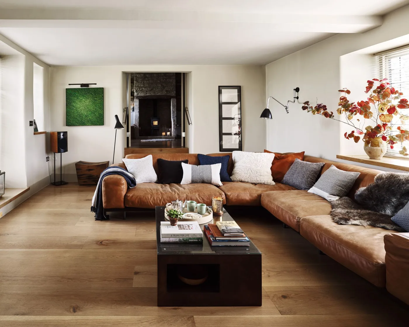 Pale living room with a brown corner sofa, neutral cushions, a small dark coffee table and a wall-mounted reading light.
