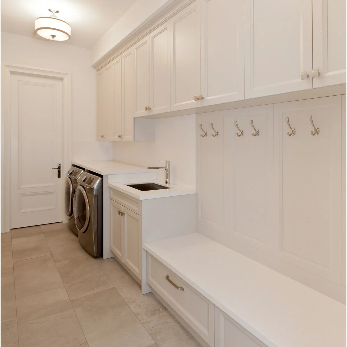 Long white laundry room with machines and a sink at the far end and a bench with hooks in the foreground