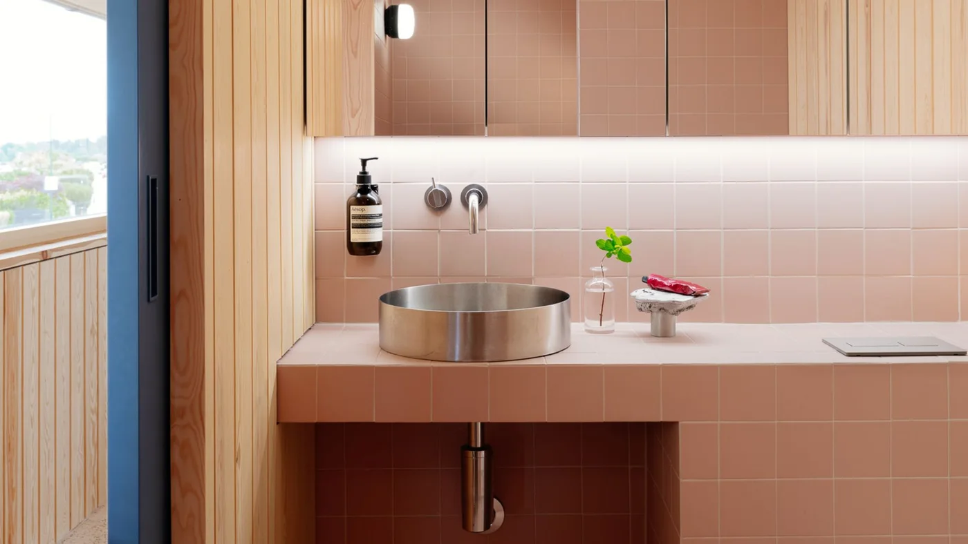 Pink square tiles surround a round metal basin beneath mirrored storage beside vertical timber wall boards.
