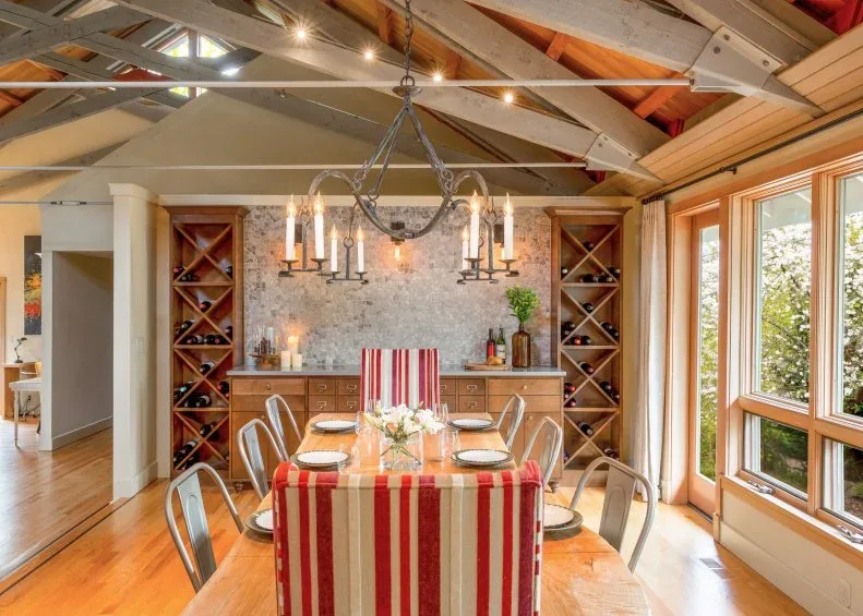 Red-and-white striped upholstered end chairs and metal side chairs around a wooden table, beside wine racks and broad windows.