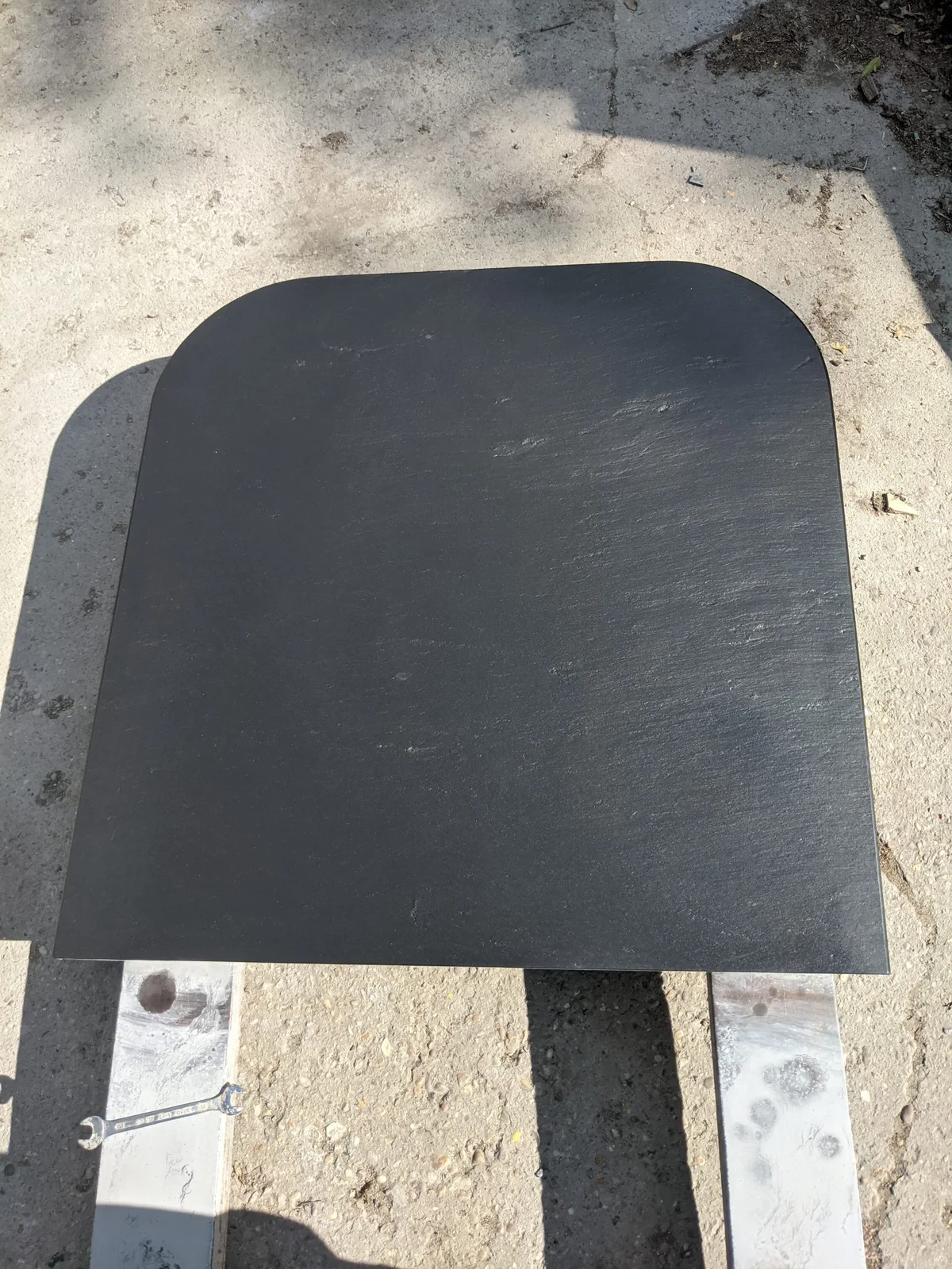 A rectangular riven slate slab with rounded front corners is photographed close up in a workshop setting.