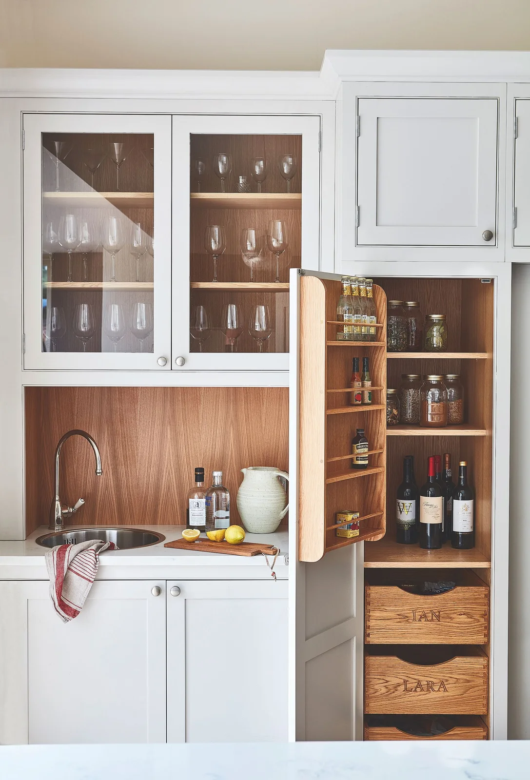 Narrow white cupboard with bottles, jars, door racks and two wooden drawers