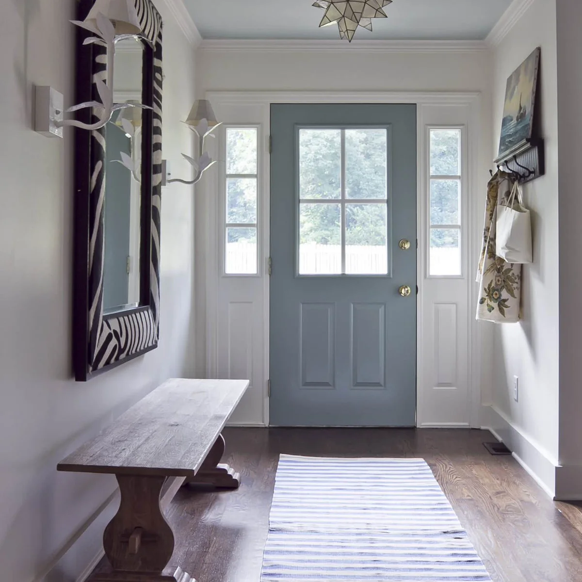 Small entrance with a blue-gray glazed door, a wooden bench, patterned mirror and wall hooks opposite.