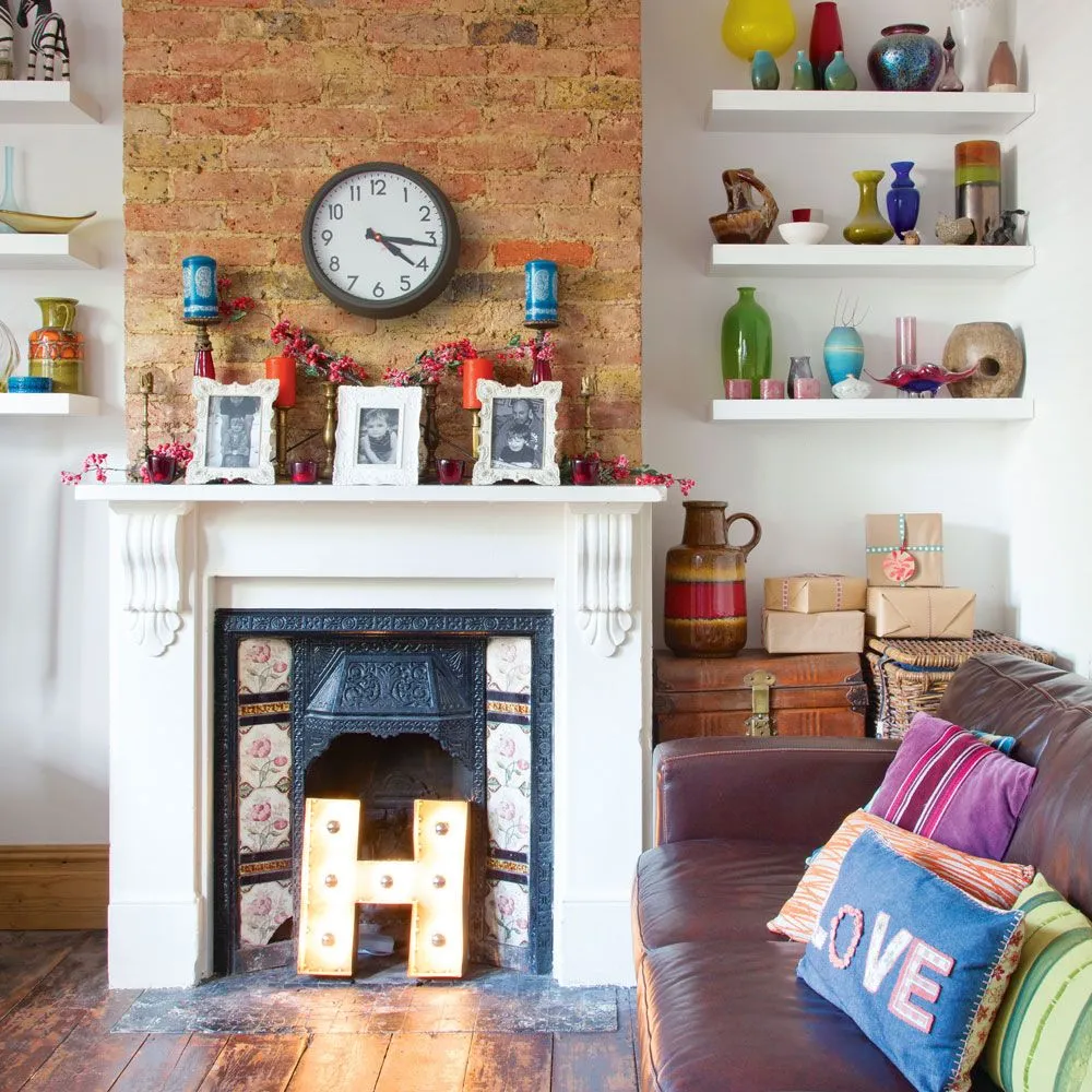 A pale mantel sits against exposed brick between shelves of colorful objects.
