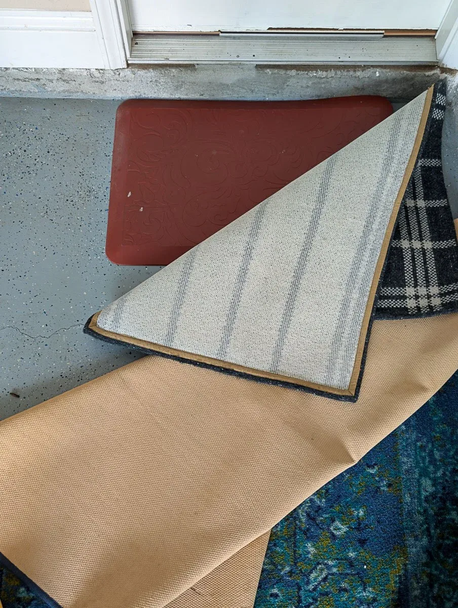Several lifted floor mats and a blue patterned rug beside a garage door threshold.