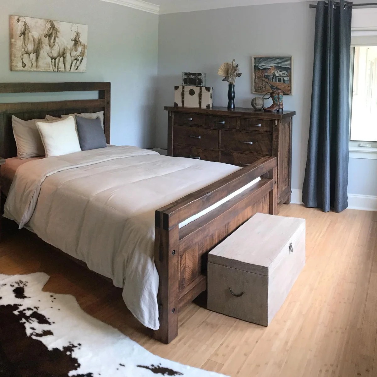 Bedroom with a dark wood bed and dresser, pale bedding, horse artwork and a spotted rug at the foot