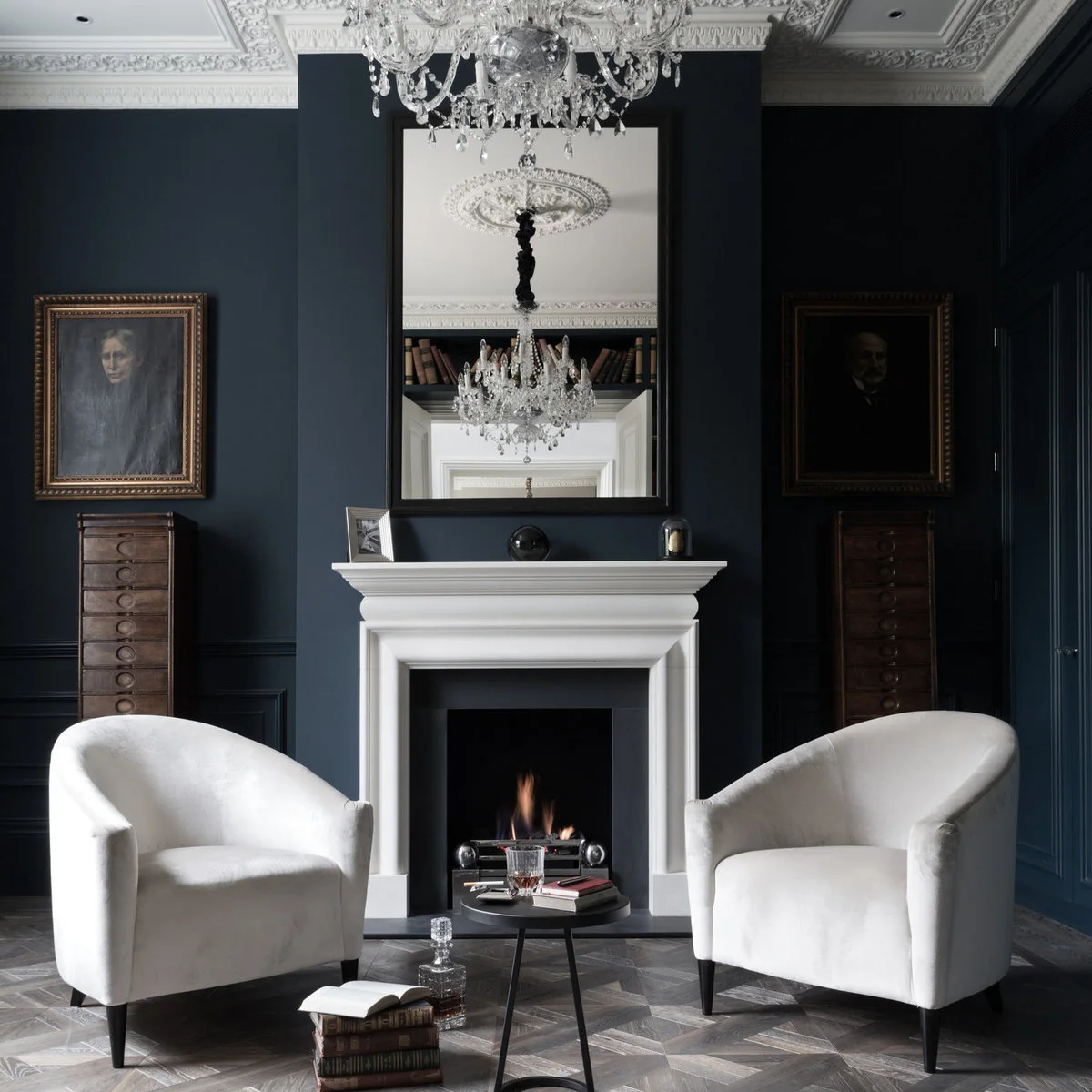 Two pale rounded chairs in front of an inky fireplace wall and tall mirror