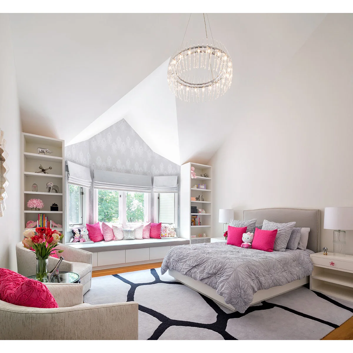 A gray window seat with bright pink pillows and white drawers in a bedroom with pale walls and pink accents.