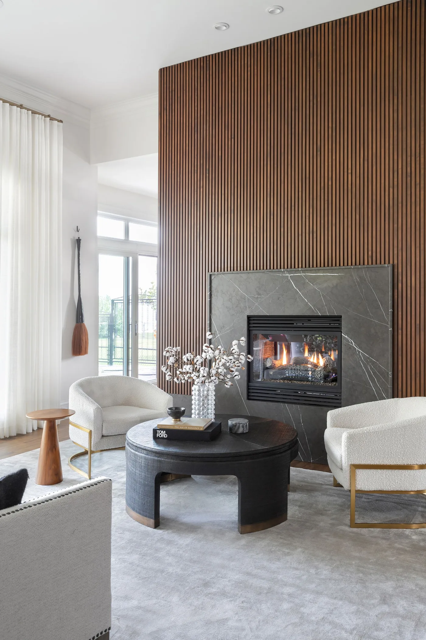 Tall wood-toned vertically lined fireplace wall with dark veined surround, pale chairs and round black table