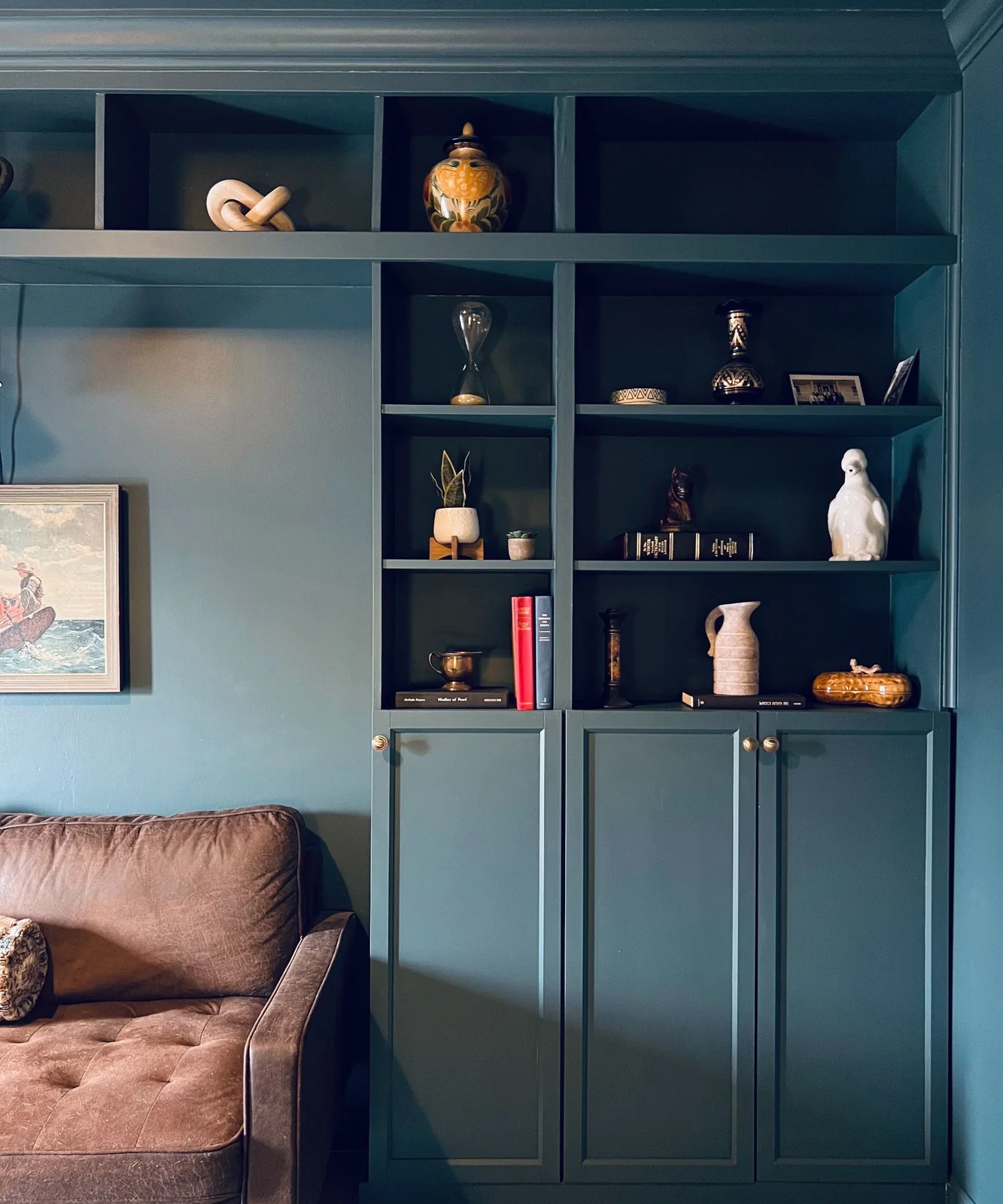 Blue-green bookcase wall with closed lower cupboards framing the edge of a brown sofa