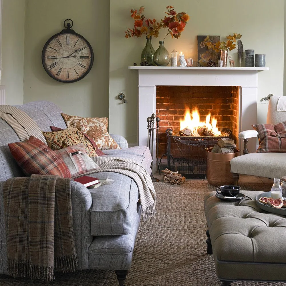 Plaid-covered seating and floral cushions surround a pale fireplace against a muted green wall