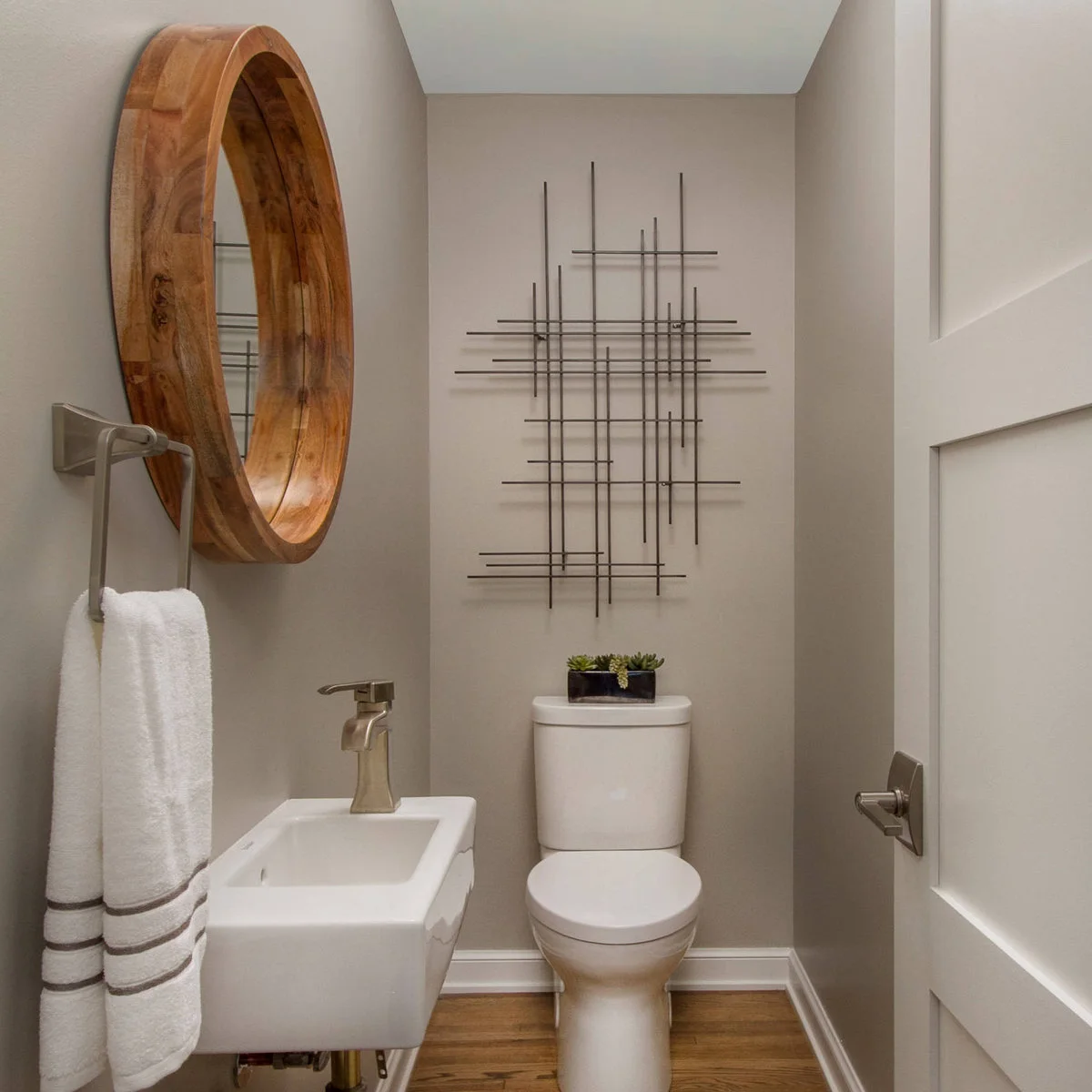 Open grid-like wall sculpture above a toilet beside a round wood-framed mirror