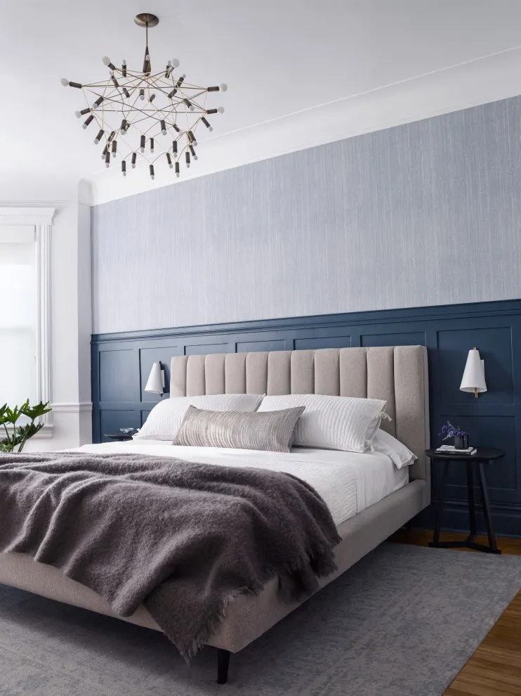 Blue-gray paneling covers the lower wall behind a bed beneath a lighter upper surface