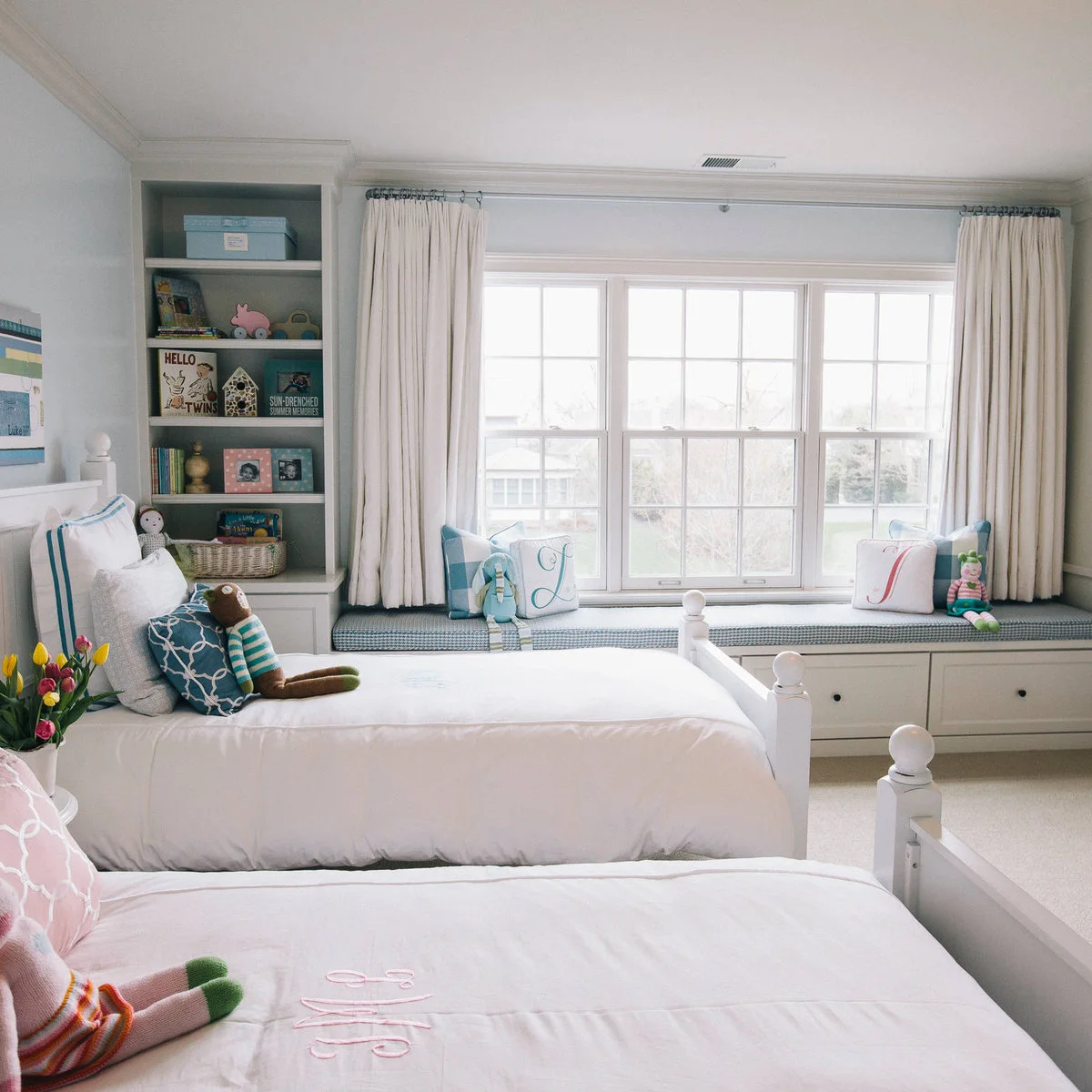 Twin bedroom with a long cushioned window seat above white storage drawers
