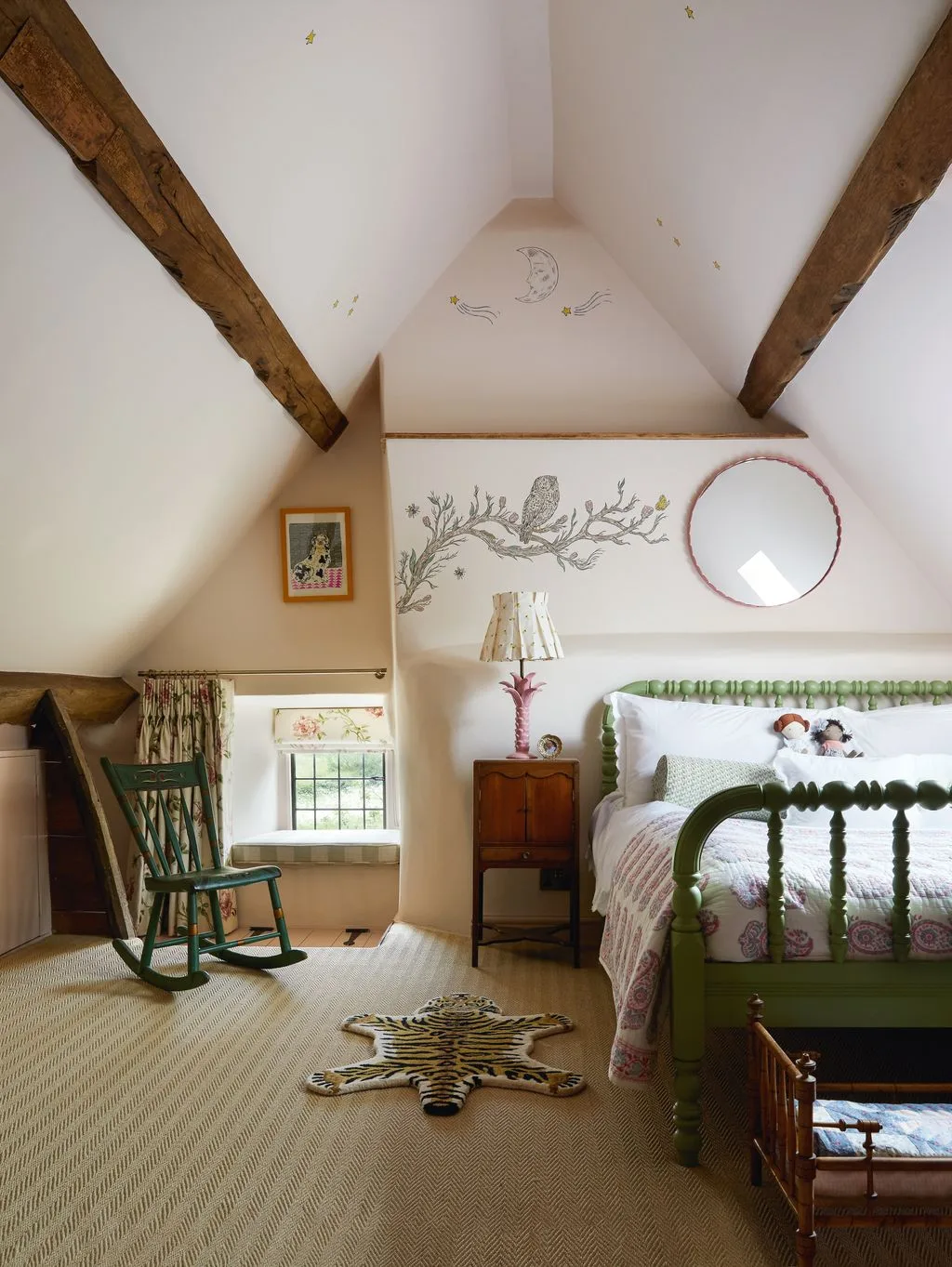 Attic bedroom with exposed sloping beams, green turned bed frame, owl wall illustration, green rocking chair and tiger-shaped rug