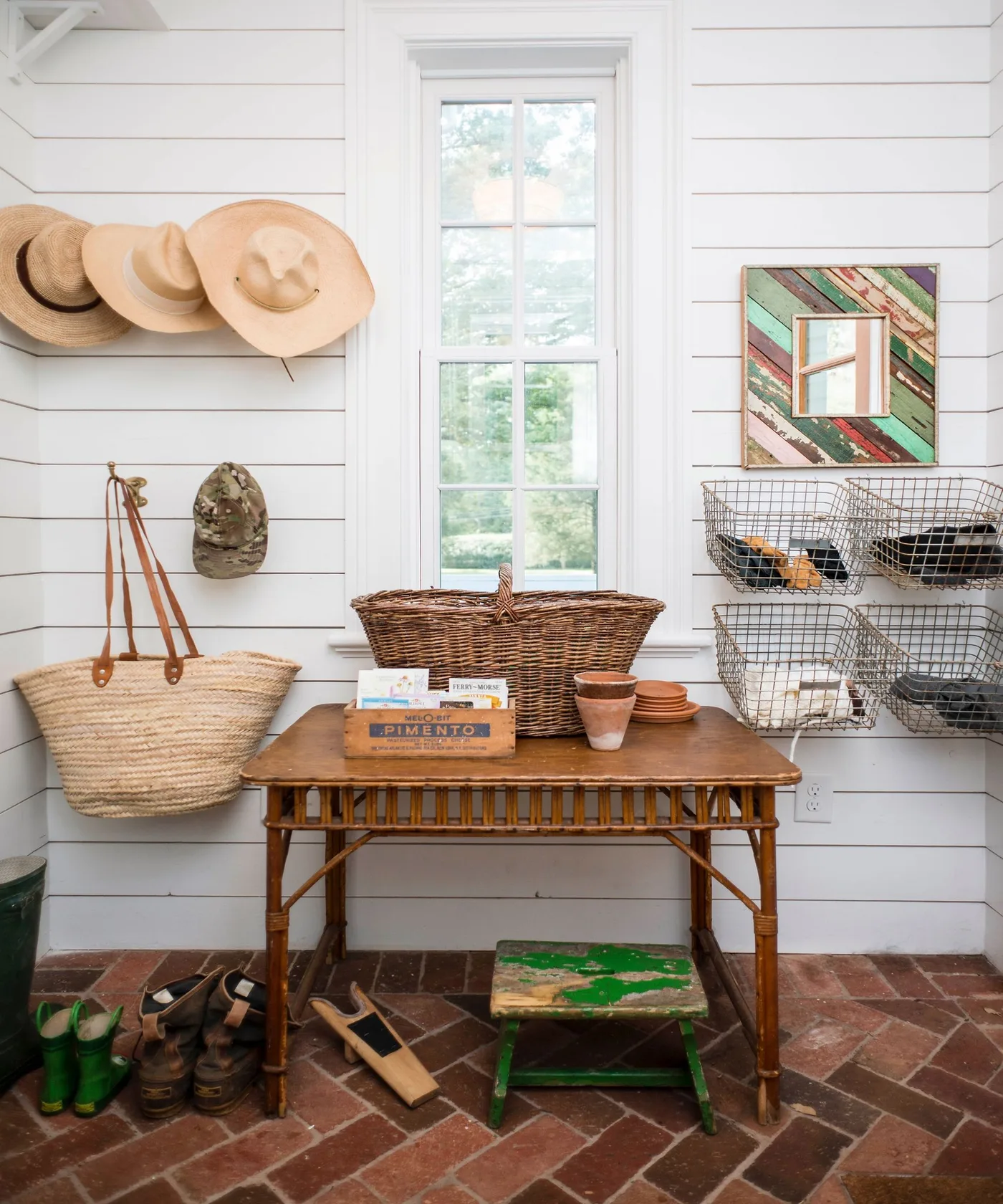 Entry with white horizontal paneling, hanging hats and woven bag, wire baskets, wood table, green stool and reddish herringbone floor