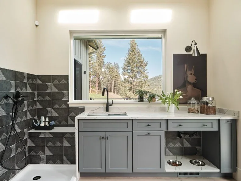 Gray mudroom sink cabinets stand beside a tiled pet-washing basin, with a recessed feeding space below one counter section.