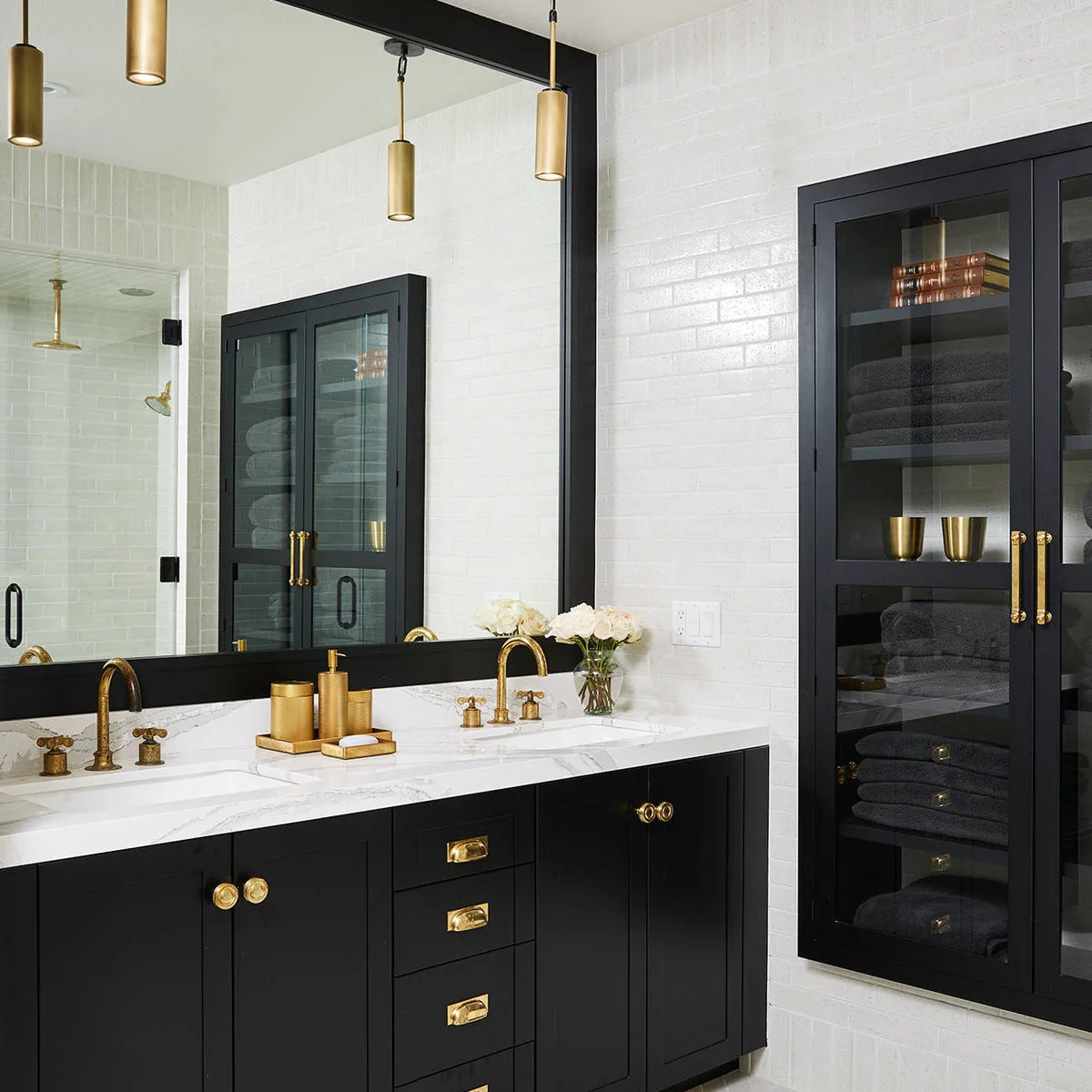 Black double vanity with gold-colored faucets, a central accessory tray and small white flowers.