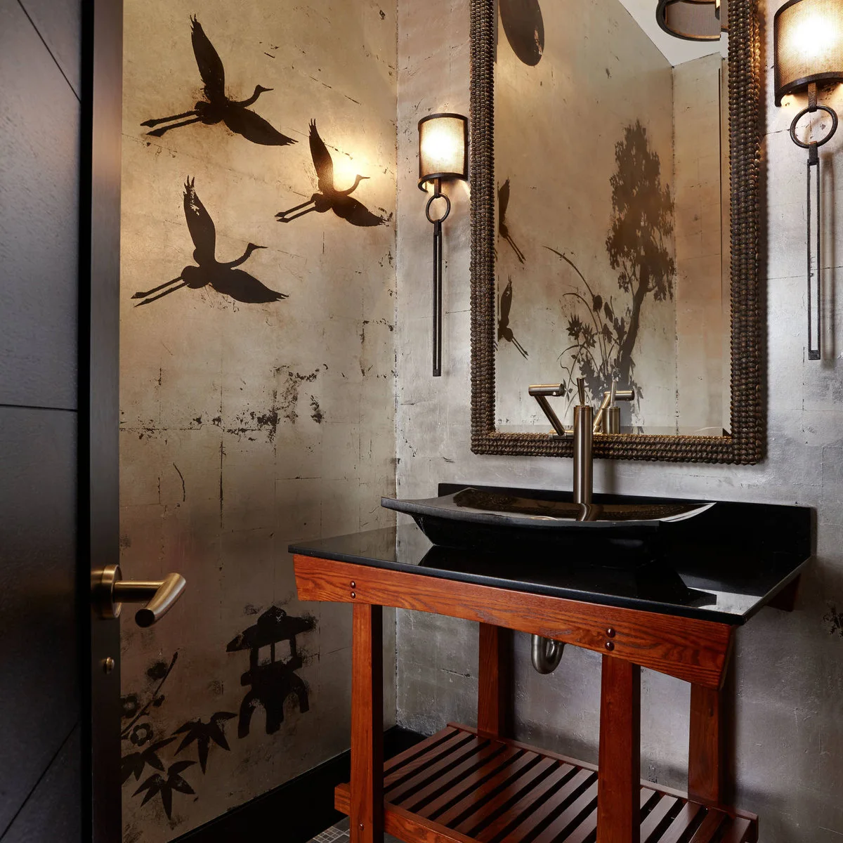 A wood console with a dark vessel basin beneath a beaded mirror, against bird-and-branch patterned walls.