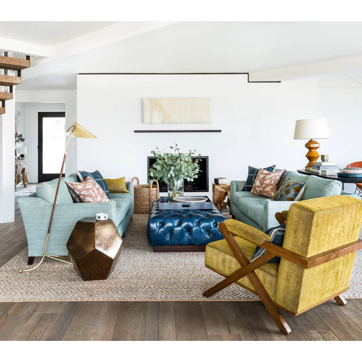 Pale blue sofas facing each other around a blue ottoman with a mustard wood-framed chair in the foreground