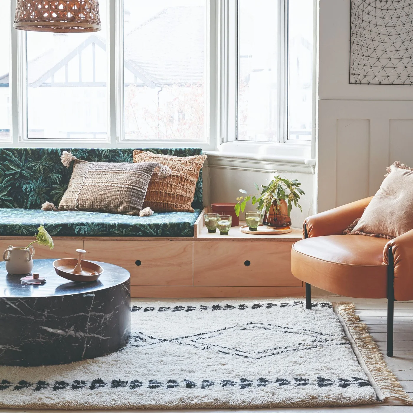 A green patterned window seat has timber drawer storage below and a clear ledge beside a tan chair.