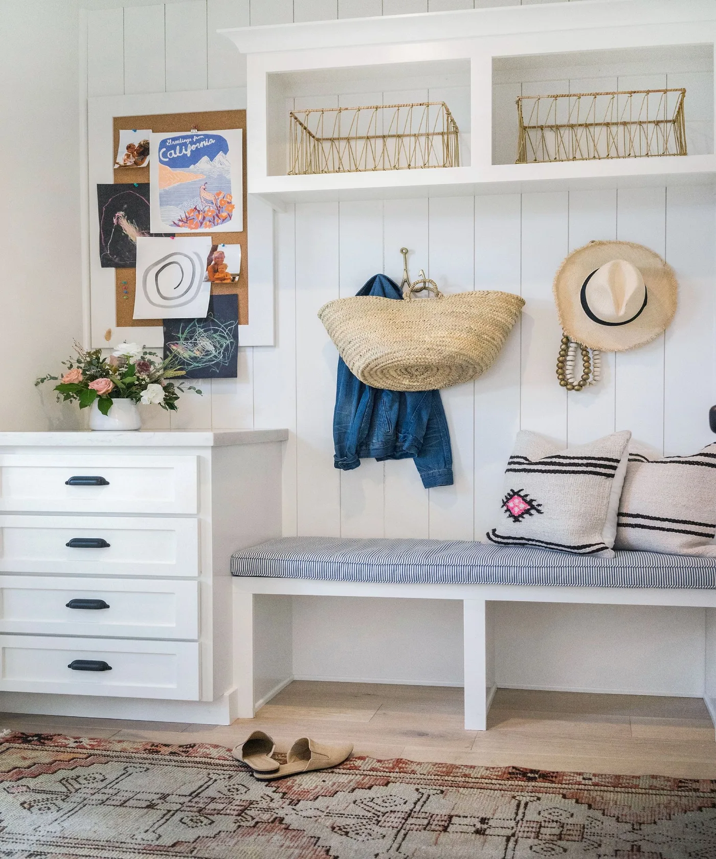White entry bench with striped cushion, upper wire baskets, wall hooks, narrow drawers, pinboard and patterned floor rug