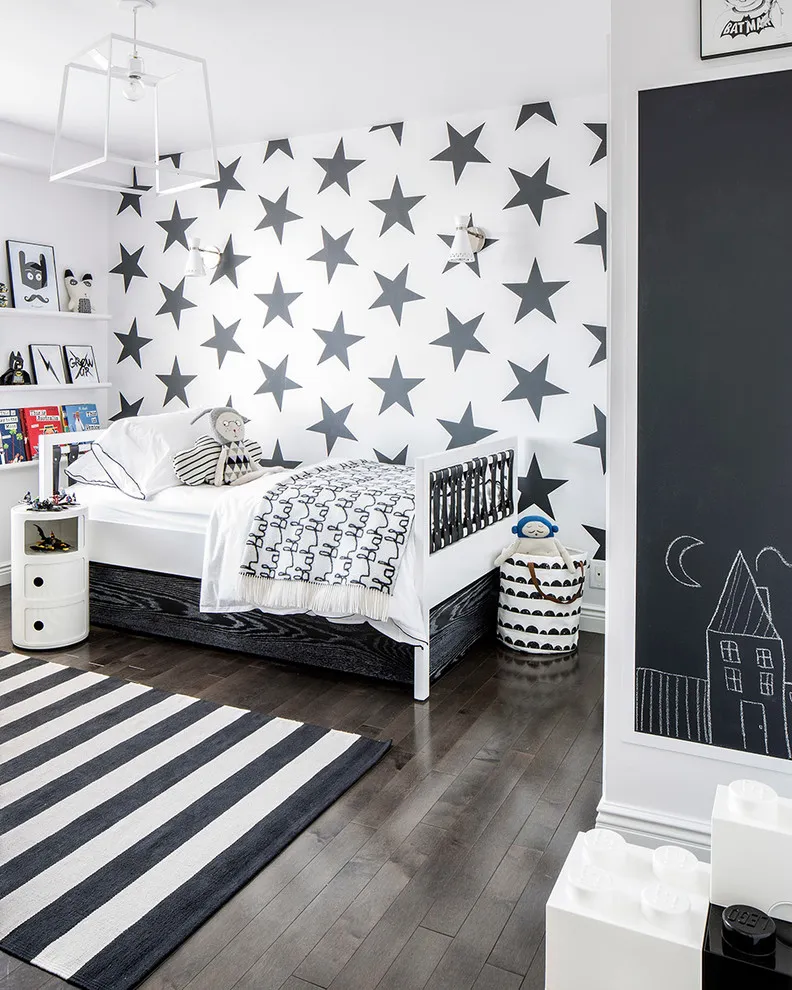 Black stars cover a white wall above pale bedding beside a striped rug