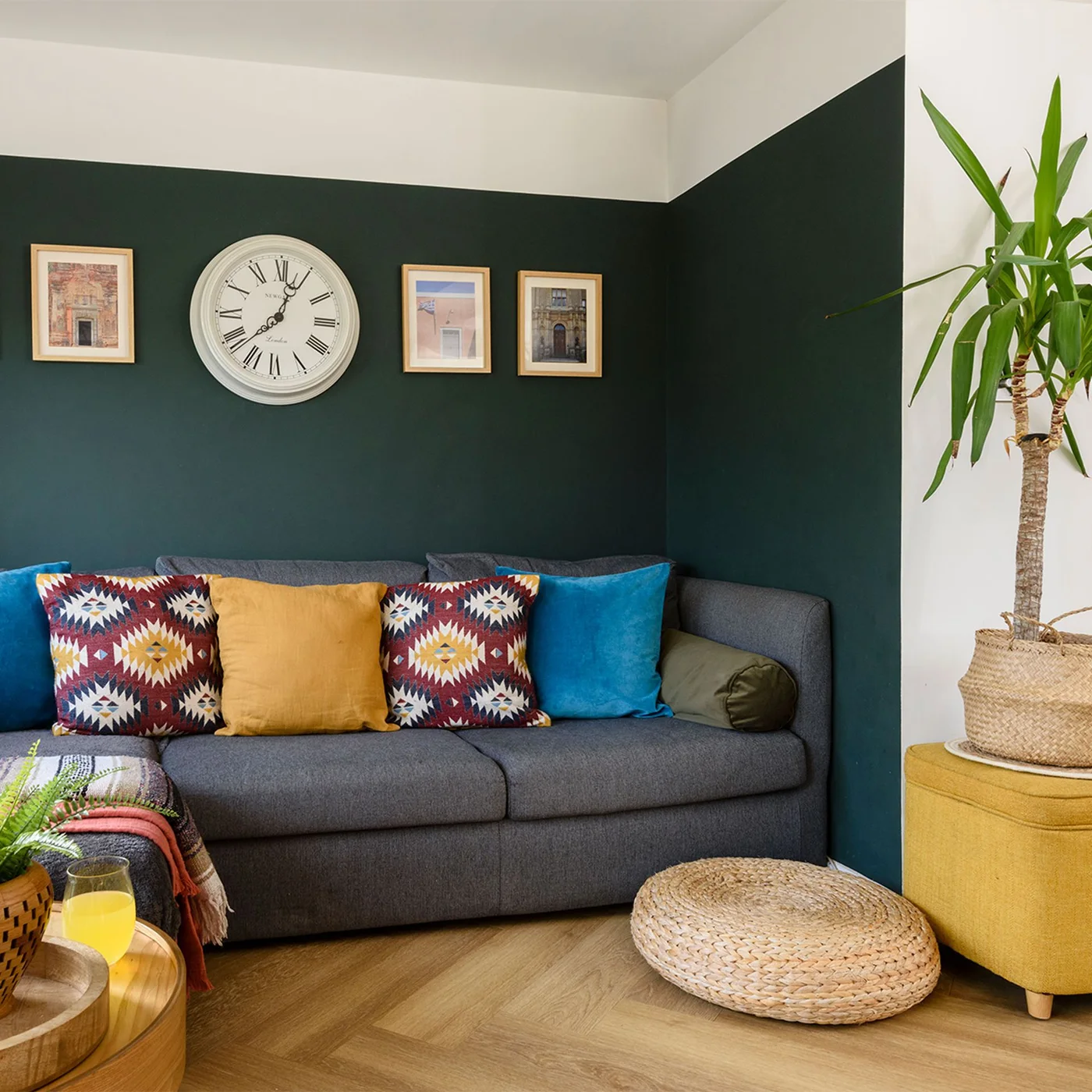 A gray sofa with colorful cushions sits against deep green lower walls below a pale upper wall and ceiling