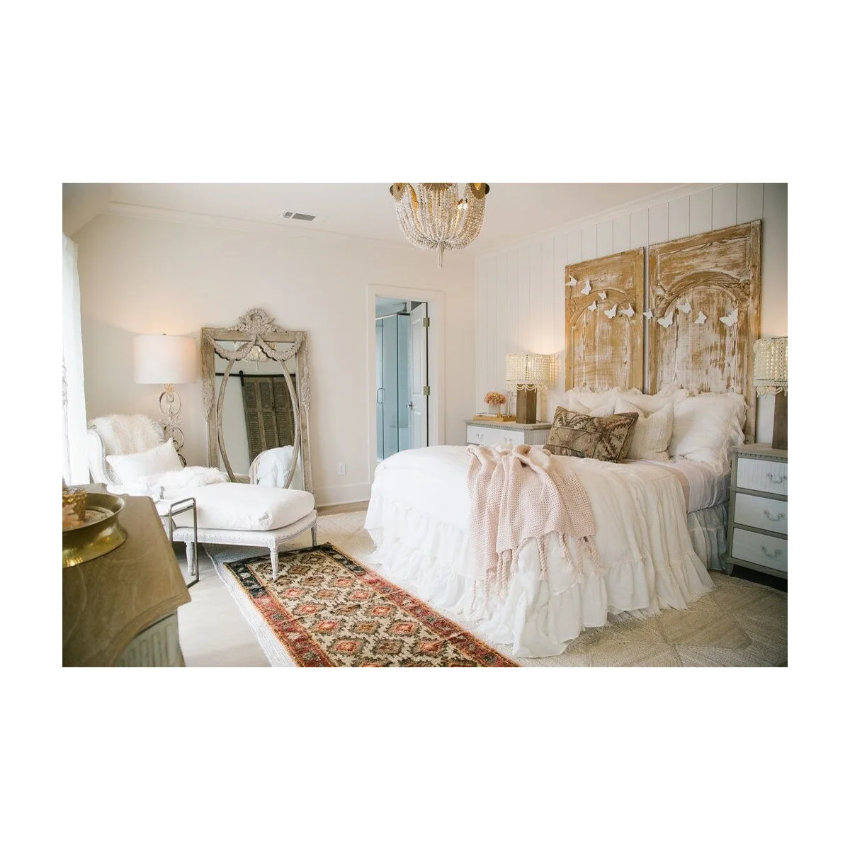 White bedroom with two worn-looking decorative panels behind the bed, pale bedding and an upholstered chair