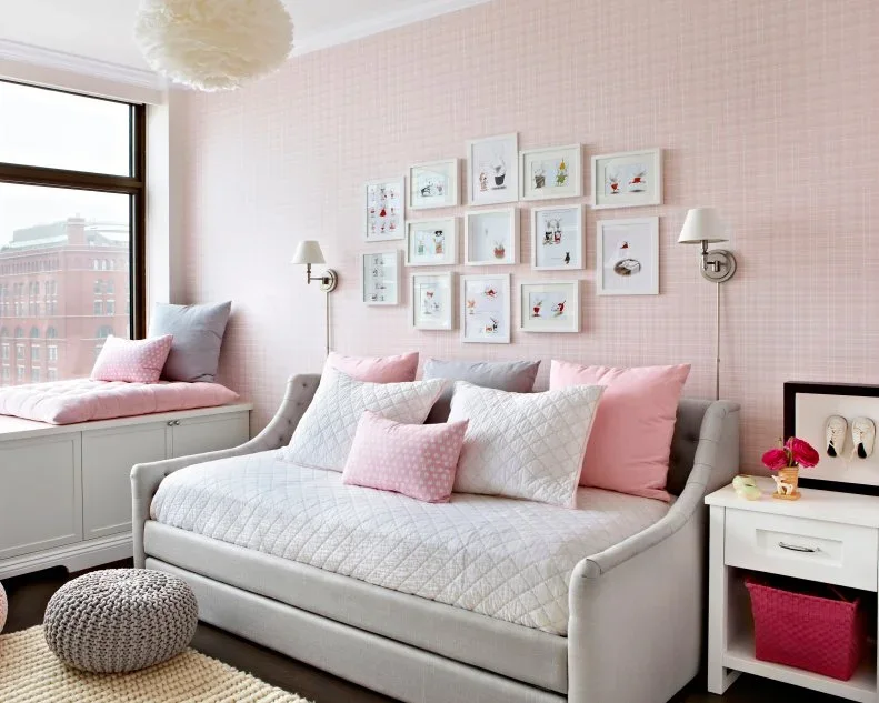 Soft pink plaid wallpaper sits behind a gray upholstered daybed, small white-framed pictures and wall lights.
