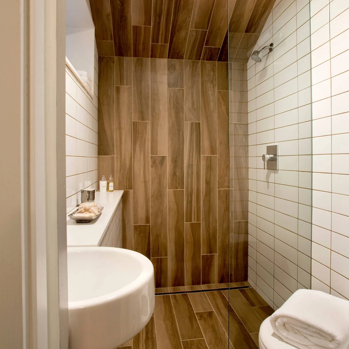 Very small bathroom with a wood-grain shower wall and sloped ceiling, white side tiles and a narrow ledge