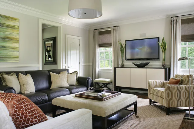 A dark leather couch faces a pale rectangular ottoman beside pale curtains and patterned armchairs